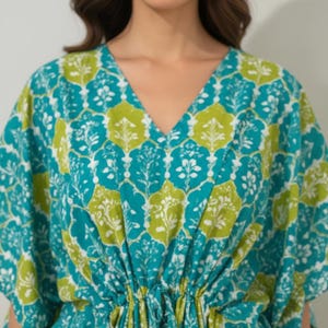 K&ouml;nnte beinhalten: T&uuml;rkis- und limettengr&uuml;nes Kaftankleid mit V-Ausschnitt und Kordelzug in der Taille. Der Stoff hat ein sich wiederholendes Blumenmuster in Wei&szlig;, Limettengr&uuml;n und T&uuml;rkis. Das Kleid hat kurze &Auml;rmel und eine lockere Passform.