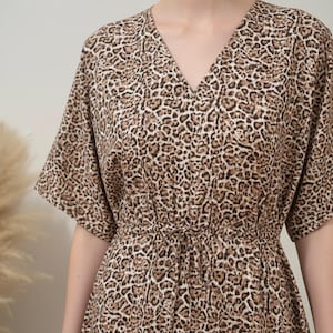 K&ouml;nnte beinhalten: Ein Kleid mit V-Ausschnitt und Leopardenmuster in Braun- und Beiget&ouml;nen. Das Kleid hat kurze &Auml;rmel und eine Kordel in der Taille. Der Stoff wirkt weich und flie&szlig;end, ideal f&uuml;r Freizeitkleidung.