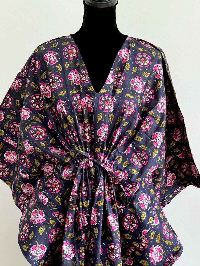 K&ouml;nnte beinhalten: Ein dunkelblauer Kaftan mit V-Ausschnitt und einem Blumenmuster in Rosa und Gr&uuml;n. Der Kaftan hat einen Kordelzug in der Taille und ist aus leichtem Stoff gefertigt.