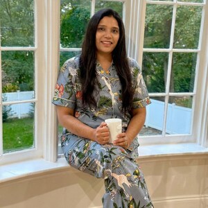 Op de afbeelding: Lichtblauwe pyjamaset met een botanische en giraffenprint. De top met korte mouwen en de broek hebben witte biezen. Een witte mok wordt in de handen gehouden. De pyjama is gemaakt van een zacht, comfortabel materiaal.