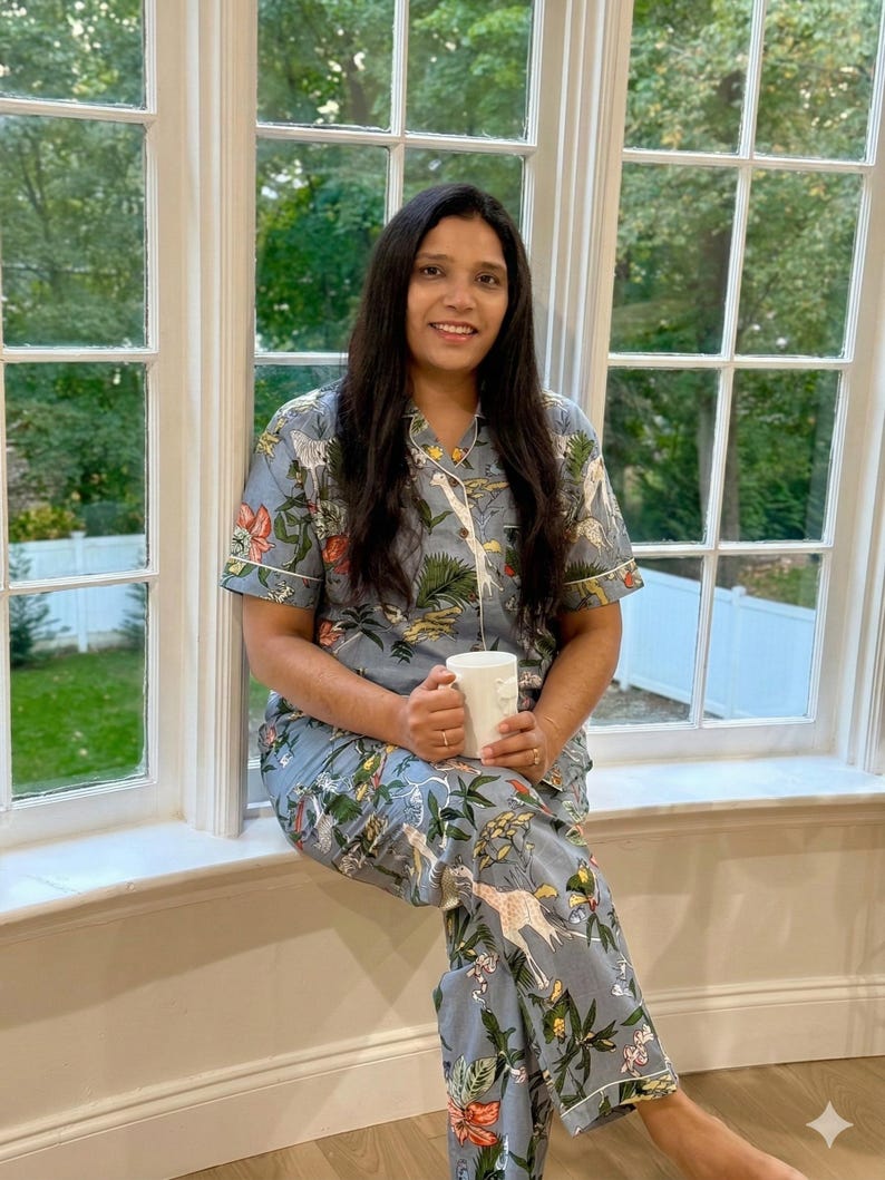 Op de afbeelding: Lichtblauwe pyjamaset met een botanische en giraffenprint. De top met korte mouwen en de broek hebben witte biezen. Een witte mok wordt in de handen gehouden. De pyjama is gemaakt van een zacht, comfortabel materiaal.