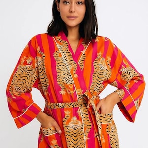 May include: A vibrant, striped robe in shades of orange and pink, featuring a tiger print. The robe has a wrap-around design with a belt, pockets, and white trim. The sleeves are wide and the overall style is relaxed and comfortable.