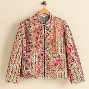 May include: A quilted jacket featuring a patchwork design of floral patterns in shades of pink, red, green, and tan. The jacket has long sleeves, a round neckline, two front patch pockets, and a black and white striped trim along the edges.