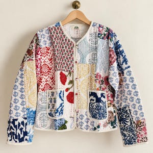 May include: A long-sleeve quilted jacket featuring a patchwork design of various floral and geometric patterns in shades of blue, red, yellow, and white. The jacket has a round neckline, a front button closure, and two square front pockets.