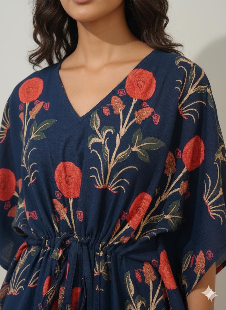 K&ouml;nnte beinhalten: Marineblaues Kaftan-Kleid mit floralem Muster. Das Kleid hat gro&szlig;e rote Blumen mit gr&uuml;nen Bl&auml;ttern und beigen Stielen. Es hat einen V-Ausschnitt und eine Taille mit Kordelzug. Die &Auml;rmel sind kurz und weit.