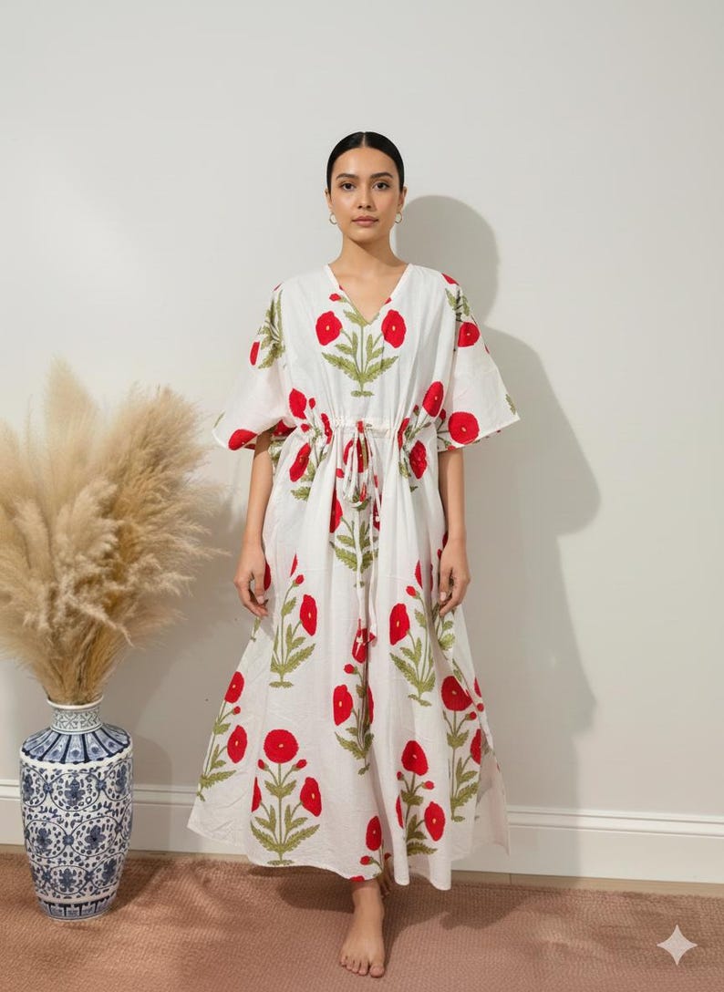 K&ouml;nnte beinhalten: Wei&szlig;es Kaftankleid mit rotem Blumenmuster und gr&uuml;nen Bl&auml;ttern. Das Kleid hat einen V-Ausschnitt, kurze &Auml;rmel und einen Kordelzug in der Taille. Der knielange Kaftan ist aus leichtem Stoff gefertigt und ideal f&uuml;r warmes Wetter.