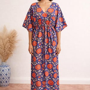 K&ouml;nnte beinhalten: Ein langes, flie&szlig;endes Kleid mit V-Ausschnitt und kurzen &Auml;rmeln. Das Kleid hat ein lebhaftes Blumenmuster in Orange und Wei&szlig; auf tiefblauem Hintergrund. Die Taille ist mit einem Kordelzug gerafft. Das Kleid ist f&uuml;r Freizeitkleidung geeignet.
