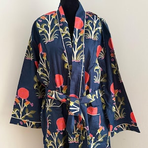 May include: A dark navy blue robe featuring a repeating floral pattern with vibrant red blossoms, green stems, and leaves. The garment includes long sleeves, a tie-waist belt, and thin white piping along the front opening and sleeve cuffs.