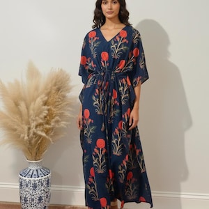 K&ouml;nnte beinhalten: Marineblaues Kaftankleid mit V-Ausschnitt und floralem Muster in Rot und Gold. Das Kleid hat eine Kordel in der Taille und kurze &Auml;rmel. Das Model tr&auml;gt goldene Sandalen.