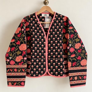 May include: A quilted jacket featuring a black base with a repeating red and white floral pattern. The garment has long sleeves, a collarless open front, and pink trim along the edges. A tag is visible at the inner neckline.