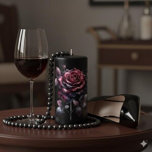 May include: A black pillar candle with a large, detailed rose design in shades of red and purple. A strand of black beads and a glass of red wine are next to the candle. A pair of black high heels is also in the image.