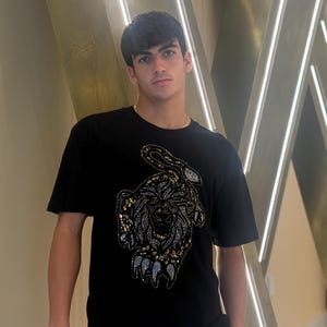 Peut inclure: T-shirt noir à manches courtes avec un motif de tigre en strass détaillé sur le devant. Le motif du tigre présente des strass dorés et argentés. Le t-shirt est de style col rond classique.