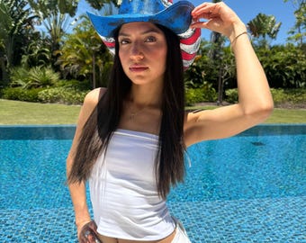 Puede incluir: Un sombrero de vaquero azul, rojo y blanco con un diseño de estrella. El sombrero tiene un ala curvada y está decorado con colores patrióticos. El sombrero es un accesorio elegante para eventos al aire libre.