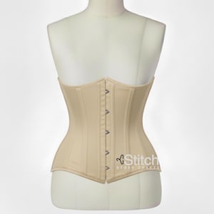 May include: A beige corset featuring a front busk closure with silver-toned metal clasps. The garment is displayed on a mannequin torso and includes the text Stitch STORY CRAFTS printed in white on the lower right side of the fabric.