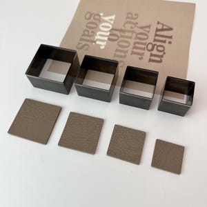 May include: Set of five black square-shaped leather craft punches, arranged in decreasing size from left to right.  Five brown leather squares are placed below the punches, each cut to the size of the corresponding punch.