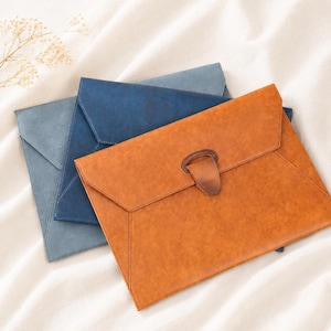 May include: Three leather document holders in shades of blue and brown. The front-most holder is a warm brown with a leather clasp. The other two are blue, with one a lighter shade than the other. The holders are rectangular with a flap closure.