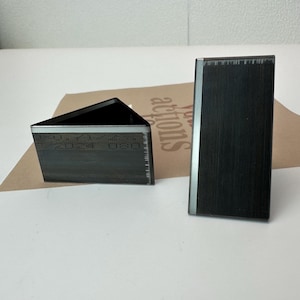 May include: Two black metal corner protectors with a silver trim. The corner protectors are in the shape of a triangle and a rectangle.