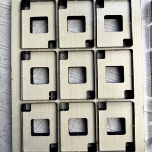 May include: A rectangular metal die featuring nine square apertures, each with a central square cut-out. The die is marked with the numbers "88*63". The metal has a light colour. The dimensions are 88mm by 63mm.