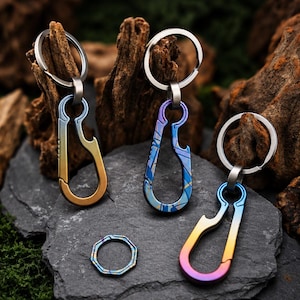 May include: Three metal carabiner keychains with integrated bottle openers, each featuring a unique gradient finish in shades of blue, gold, and purple, accompanied by a small, separate octagonal metal ring, all displayed together as a set.