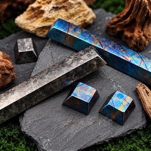 May include: Two long, rectangular metal bars and three small, square-based pyramid keycaps. One bar and one keycap feature a mottled gray, metallic finish. The other bar and two keycaps display an iridescent blue, gold, and purple finish.