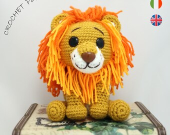 May include: Crocheted lion amigurumi toy with orange and yellow yarn for the mane, brown eyes, and a brown nose. The toy is sitting on a vintage suitcase with the text "CRISTINASAMIGURUMI" on the side.