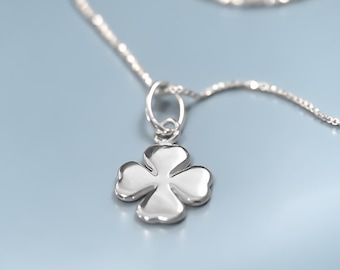 May include: A polished silver-tone necklace featuring a four-leaf clover pendant. The pendant is suspended from a delicate, thin metal chain. The surface of the clover charm is smooth and reflective, catching the light with a bright metallic sheen.