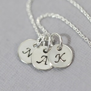 May include: Silver necklace with three round charms, each engraved with a letter: N, A, and K.