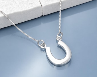 May include: A polished silver-tone horseshoe pendant suspended from a delicate box chain necklace. The horseshoe is oriented with the opening facing upward and is attached to the chain by two small circular jump rings on either side.