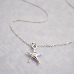 May include: A silver starfish pendant necklace. The starfish charm is suspended from a delicate chain. The necklace is a simple, elegant piece of jewelry. The starfish is a bright, shiny silver color.