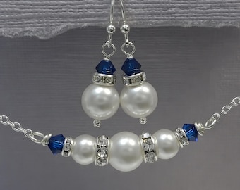May include: A jewelry set consisting of a necklace and a pair of drop earrings. Each piece features white faux pearls, deep blue crystal bicones, and silver-toned rhinestone rondelle spacers, all connected by a silver-toned metal chain.