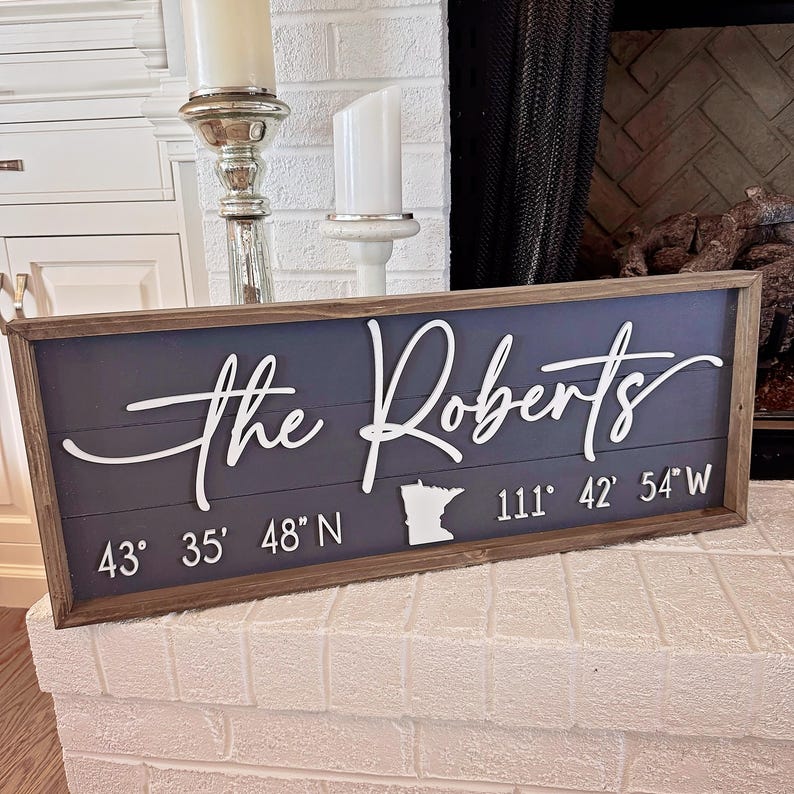 K&ouml;nnte beinhalten: Ein graues Holzschild mit dem Text "The Roberts" in wei&szlig;er Kursivschrift. Das Schild enth&auml;lt auch die Koordinaten "43&deg; 35' 48" N 111&deg; 42' 54" W" und eine Umrandung des Bundesstaates Minnesota.