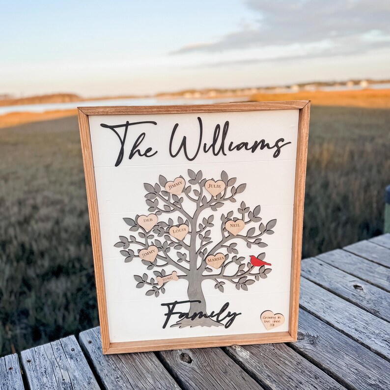 May include: A wooden sign with a gray tree and hearts with names on them. The sign says "The Williams Family" and has a red cardinal on a branch.
