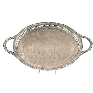 Puede incluir: Una bandeja de servicio ovalada de tono plateado con un intrincado patrón floral grabado en la superficie central. La bandeja presenta un borde elevado y calado con un diseño de cuerda y dos asas curvas y ornamentadas.