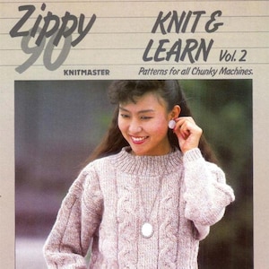 May include: A woman wearing a light purple cable-knit sweater with a high neckline and long sleeves. The sweater has a textured pattern and is paired with a pendant necklace. The image also features text that reads "Zippy 90" and "Knit & Learn Vol. 2".