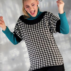 May include: A black and white houndstooth patterned sweater with a high neckline and long teal ribbed sleeves. The sweater features a black collar and hemline, paired with a black bow hair accessory and black pants, creating a layered look.