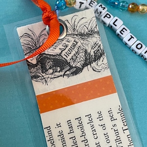 May include: A handmade bookmark featuring a vintage illustration of a rat and the word "HUMBLE". The bookmark has an orange ribbon and a beaded strand spelling "TEMPLETON". The text on the bookmark reads "grass behind...a deviled ham...The rat crawled..."