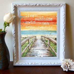 May include: A framed print featuring a watercolour background of a beach scene with a wooden walkway leading to the sea. The quote "live in the sunshine swim the sea drink the wildair ralph waldo emerson" is printed on the background.