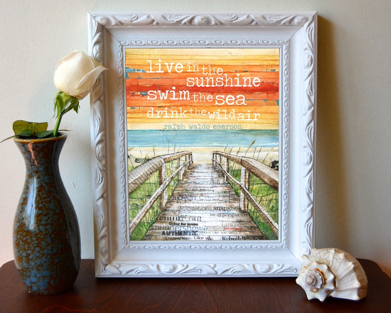 May include: A framed print featuring a watercolour background of a beach scene with a wooden walkway leading to the sea. The quote "live in the sunshine swim the sea drink the wildair ralph waldo emerson" is printed on the background.