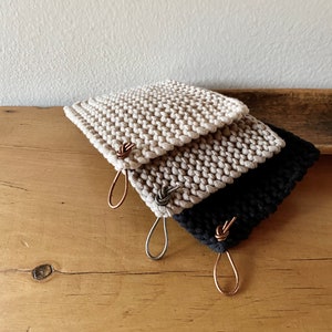 May include: Three knitted pot holders with leather loops. The pot holders are beige, light brown, and black.