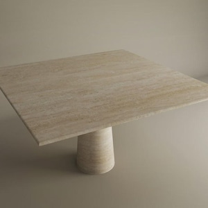 May include: A square, light-colored stone table with a single, cylindrical base. The tabletop is approximately 48 inches wide and has a natural, textured appearance. The table is suitable for indoor use.