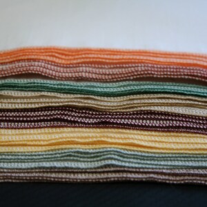May include: A stack of folded fabric cloths in various colours, including orange, green, brown, and yellow. The cloths have a decorative stitched edge.