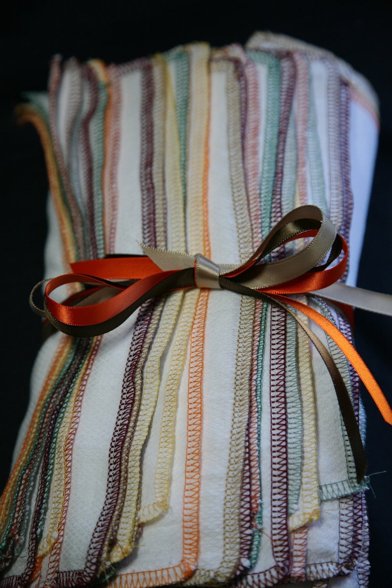 May include: A stack of white fabric squares with colourful stitched edges, tied together with a brown and orange ribbon bow.