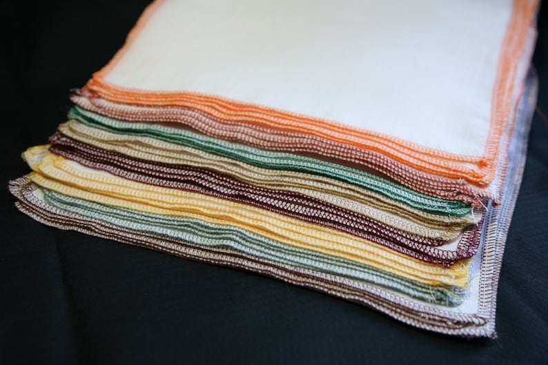 May include: A stack of colourful fabric squares in a variety of colours, including orange, green, brown, and yellow. The fabric squares are folded neatly and have a stitched edge.