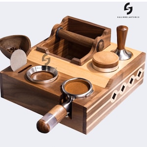 Puede incluir: Estación de espresso de madera con varios compartimentos y accesorios. Incluye un soporte para portafiltro, un tamper y un cuenco pequeño. La madera tiene un acabado natural con detalles en madera clara y oscura. La marca "SQUIRRELARTDECO" es visible.