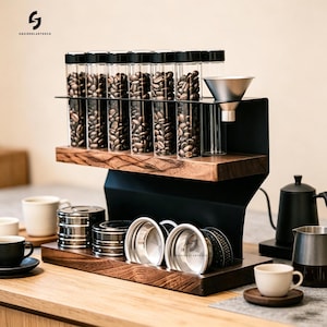 Puede incluir: Una estación de almacenamiento y preparación de café de dos niveles con marco de metal negro y estantes de madera oscura. El estante superior contiene seis tubos de vidrio transparente con granos de café y un embudo plateado. Abajo hay botes.