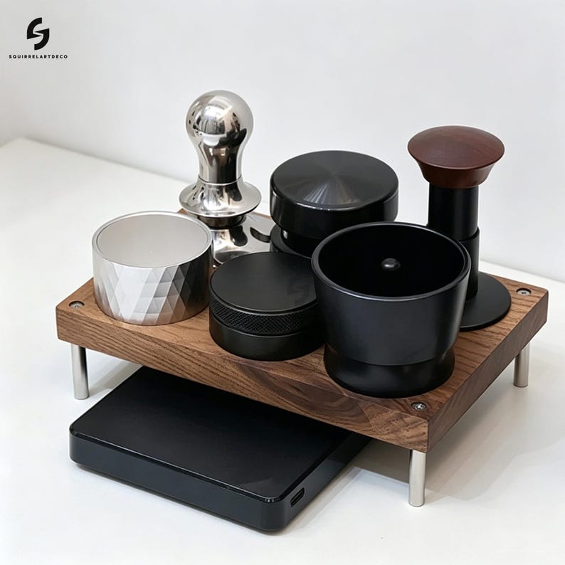 Op de afbeelding: Een houten standaard met vier zilveren poten bevat een verzameling espresso-accessoires, waaronder een zilveren tamper, een zilveren doseerring, een zwarte distributeur, een zwarte doseertrechter en een zwarte tamper met een donkerhouten handvat.