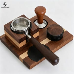 Puede incluir: Una estación de café espresso de madera con base de nogal oscuro y arce claro. El conjunto incluye un portafiltros de acero inoxidable con mango de madera oscura, un prensador de madera con base metálica y un distribuidor de café negro.