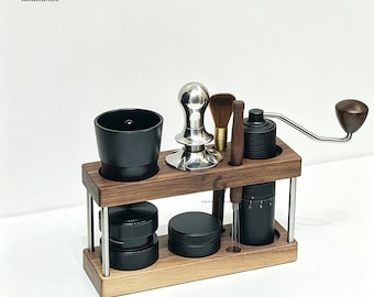 May include: A two-tiered walnut wood coffee station organiser holding a black dosing cup, a silver metal tamper, a brown bristle brush, a thin wooden stirring tool, and a black manual coffee grinder with a wooden handle and metal crank arm.
