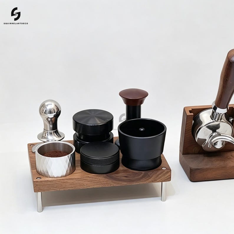 Op de afbeelding: Een houten espresso-accessoirestation met vier metalen poten met een zilveren doseerbeker met ruitpatroon en koffiedik, een zilveren tamper, twee zwarte koffieverdelers en een zwarte trechter. Een houten filterdragerstandaard staat ernaast.