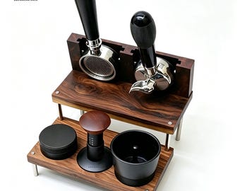 May include: A two-tiered wooden espresso station organiser featuring a dark wood grain finish. The top tier holds two metal portafilters with black handles. The bottom tier contains a black circular container, a wooden tamper, and a black cup.